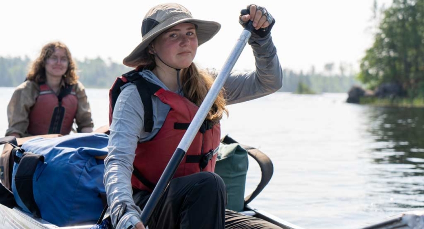 Two people in a canoe on calm water smile for a photo